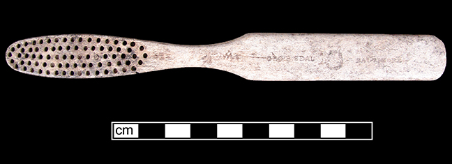 Bone toothbrush with oval head and flat handle.  The brush is missing the bristles.
